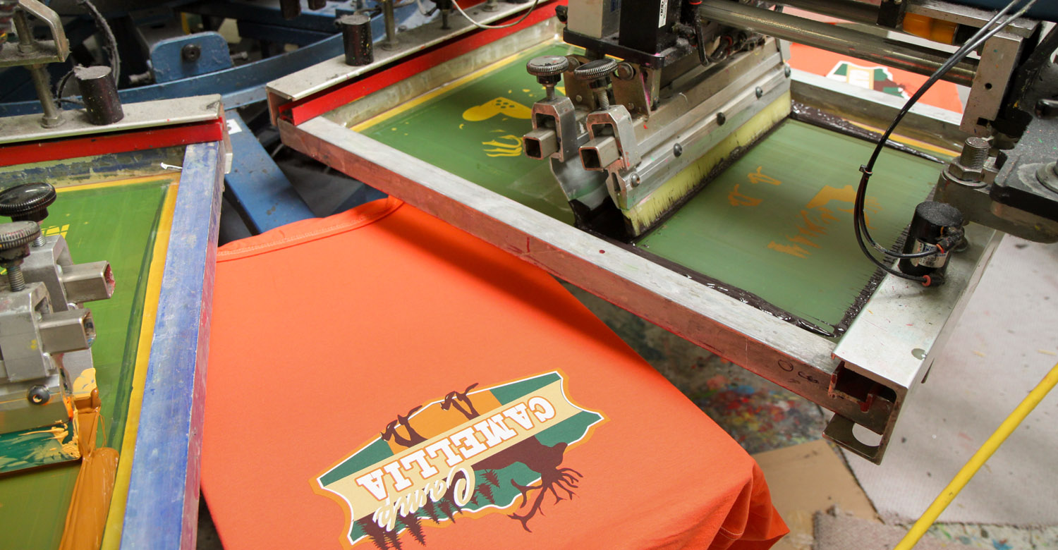 T-shirts make their way through a semi-automated screen printing press.