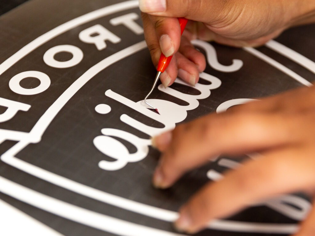 An employee weeds (removes) unused vinyl from a design.