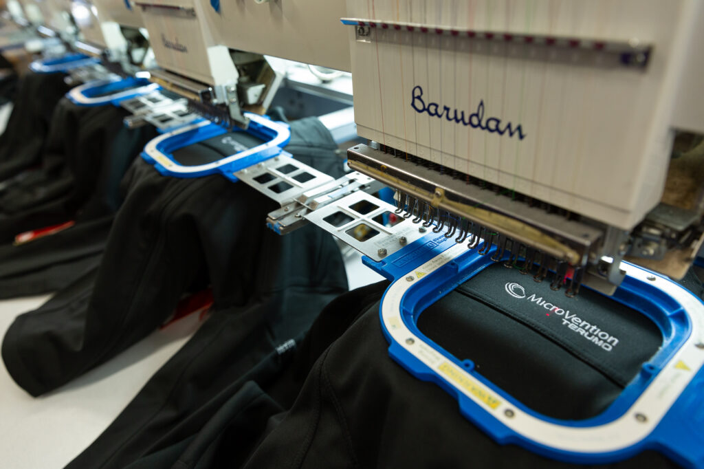 A six-head embroidery machine embroiders a corporate logo onto jackets.