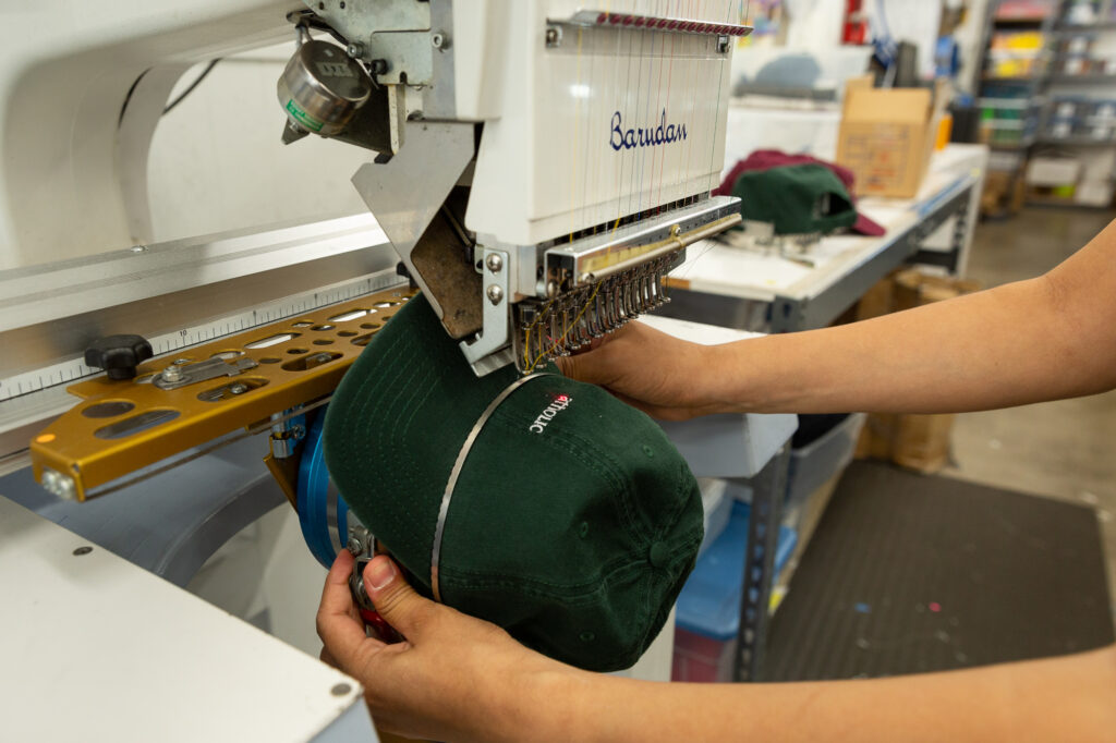 An employee places a hat on an embroidery machine.